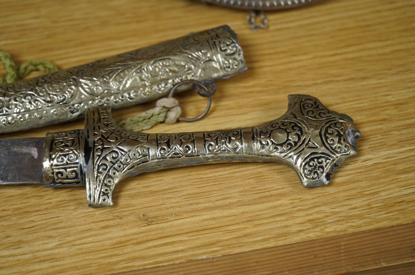 An Omani silver spice box in the form of a curved powder flask, together with a Moroccan dagger Jambiya with nickel hilt and sheath, both 20th century. Condition - fair.
